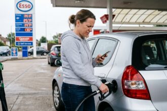 Femme comparant les prix de carburant sur son smartphone à la pompe d'une station-service