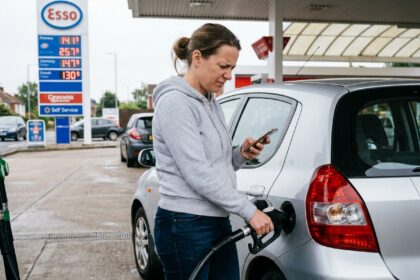 Femme comparant les prix de carburant sur son smartphone à la pompe d'une station-service